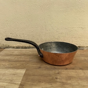 May include: A small copper saucepan with a black iron handle. The saucepan has a hammered finish and is slightly tarnished.