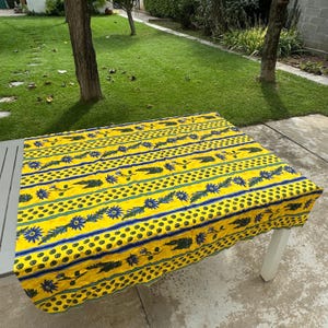 May include: Yellow tablecloth with a blue and green floral pattern. The tablecloth has a striped design with small yellow dots.