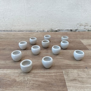 Puede incluir: Una colección de 14 pequeñas macetas de cerámica blanca, dispuestas en un patrón escalonado sobre una superficie de madera.