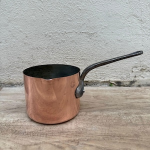May include: A small copper saucepan with a black metal handle. The saucepan has a shiny copper finish and is ideal for making sauces or melting chocolate.
