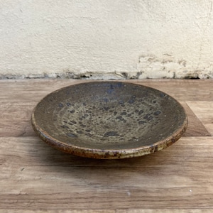 Może przedstawiać: Mała, okrągła, brązowa ceramiczna miseczka z kropkowanym szkliwem. Miseczka ma lekko uniesiony brzeg i gładką, równą powierzchnię.