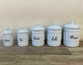 May include: Set of five white ceramic canisters with black lettering. The canisters are labeled "spices", "the", "farine", "cafe", and "sucre".