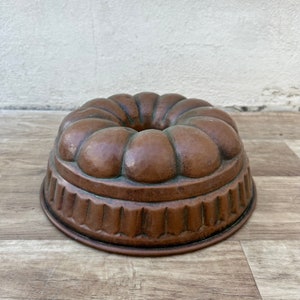 May include: A vintage copper bundt cake pan with a fluted edge and a raised, rounded center. The pan has a patina of age and use.