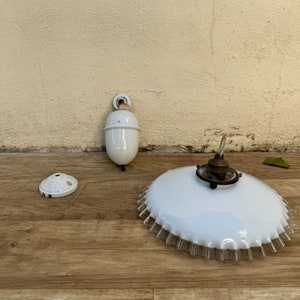 Könnte beinhalten: Drei weiße Porzellan-Leuchtenteile. Eine runde Deckenplatte, ein glockenförmiger Anhänger und ein großer, gewellter, weißer Glasschirm.