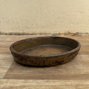 Puede incluir: Un plato ovalado de cerámica marrón con una superficie texturizada. El plato tiene un borde ligeramente elevado y un esmalte marrón oscuro.