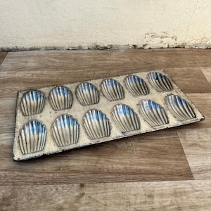 May include: A vintage silver-colored metal baking pan with 12 individual molds shaped like seashells. The pan is designed for making madeleines.