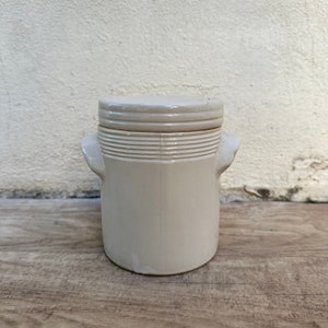 May include: A white ceramic jar with a lid and two handles. The jar has a ribbed design around the middle.