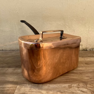 May include: A vintage copper pot with a lid and a black handle. The pot is oval shaped and has a shiny copper finish.