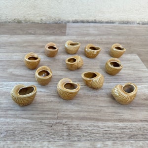 May include: Twelve small, brown ceramic pots shaped like seashells. The pots are arranged in a circle on a light brown wooden surface.