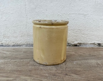 May include: A vintage, cream-colored ceramic jar with a slightly rough texture. The jar has a simple, cylindrical shape and a slightly flared rim.