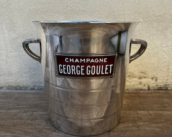 May include: Silver champagne bucket with two handles and a red and white label that reads "Champagne George Goulet".
