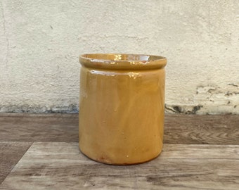 May include: A yellow ceramic jar with a smooth, glazed finish. The jar is cylindrical in shape and has a slightly rounded bottom.