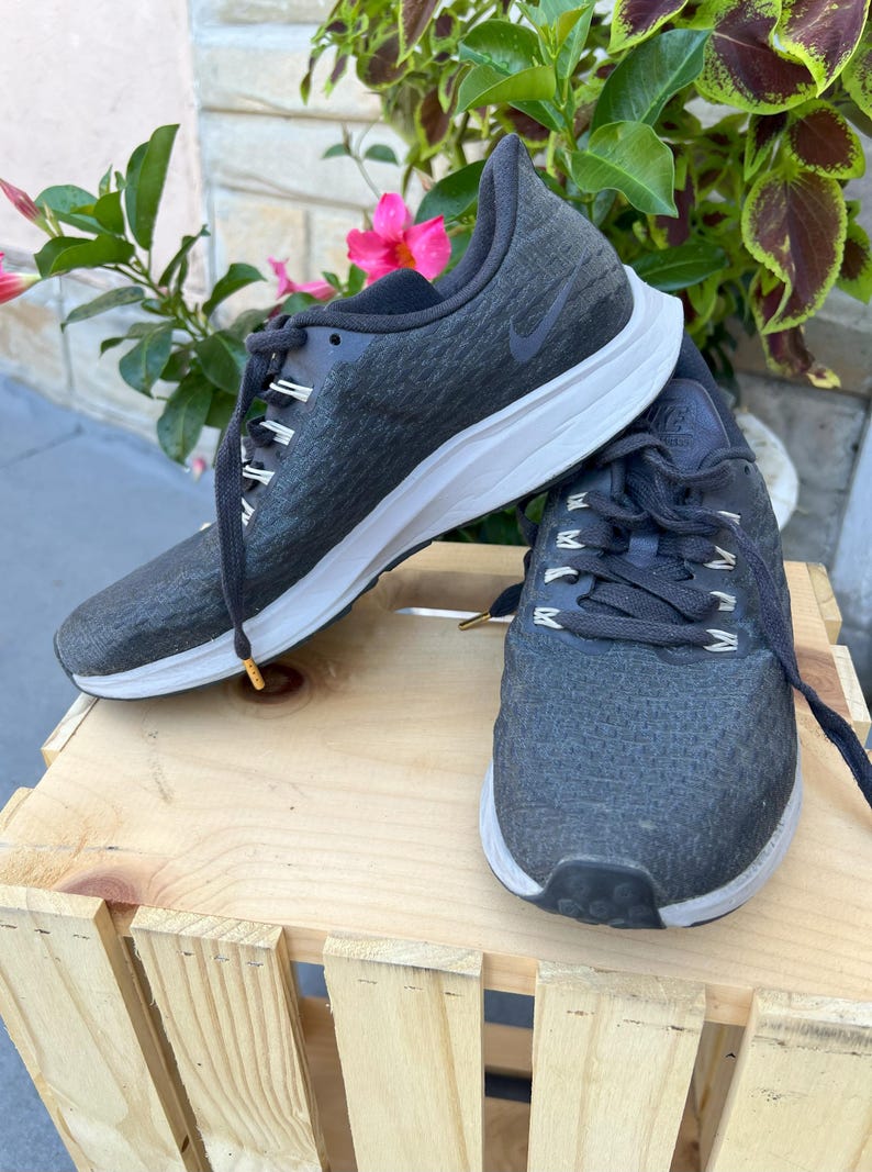 K&ouml;nnte beinhalten: Ein Paar schwarze Nike Laufschuhe mit wei&szlig;en Sohlen. Die Schuhe haben ein Obermaterial aus strukturiertem Stoff und ein schwarzes Nike Swoosh Logo an der Seite.