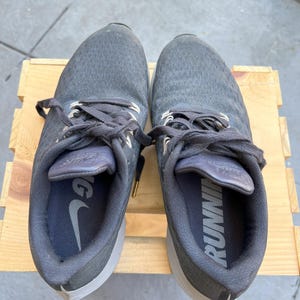 K&ouml;nnte beinhalten: Ein Paar graue Nike Laufschuhe mit schwarzen Schn&uuml;rsenkeln und einer wei&szlig;en Sohle. Die Schuhe haben das Wort "RUNNING" auf der Innenseite des rechten Schuhs aufgedruckt.