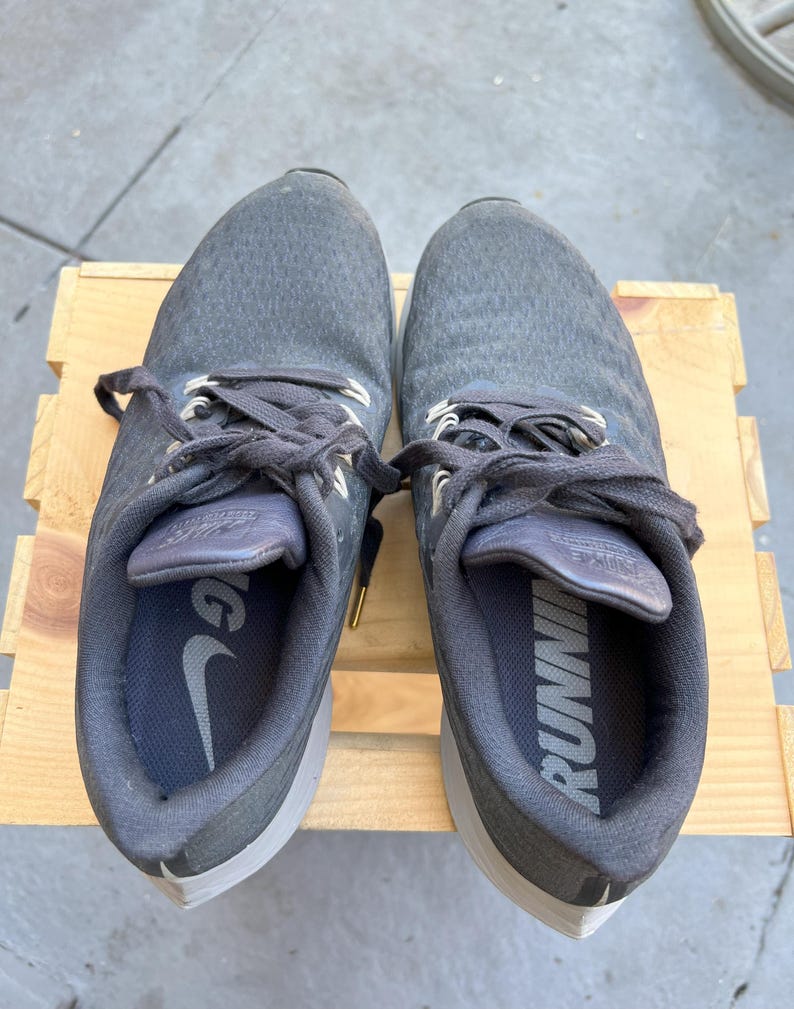 K&ouml;nnte beinhalten: Ein Paar graue Nike Laufschuhe mit schwarzen Schn&uuml;rsenkeln und einer wei&szlig;en Sohle. Die Schuhe haben das Wort "RUNNING" auf der Innenseite des rechten Schuhs aufgedruckt.