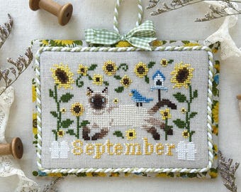 May include: A cross-stitched September 2025 calendar featuring a Siamese cat, sunflowers, and a bluebird. The calendar is framed with a green and yellow floral pattern and a green gingham bow. The text "Monthly Kitty Calendar Series 2025" is at the top.