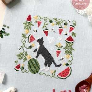 以下が含まれることがあります： スイカを持った白黒の猫が、スイカの切り身、ミツバチ、花に囲まれているクロスステッチパターン。パターンは薄いブルーのリネン生地に施されています。画像の下部には「Stitch with Coffee」というテキストとウェブサイトのアドレスがあります。