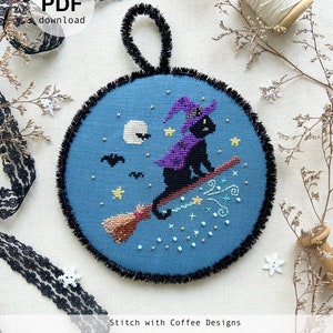 Può includere: Uno schema di ricamo a punto croce con un gatto nero che indossa un cappello da strega viola e un mantello, volando su una scopa contro un cielo notturno blu con stelle e una luna. Lo schema è intitolato "Fright Night I: Witchy" e include il sito web "www.stitchwithcoffee.etsy.com".