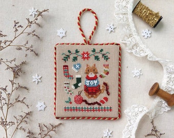 May include: Cross stitch ornament featuring a fox wearing a red and white Christmas sweater with the word "JOY" on it. The ornament is surrounded by snowflakes and other Christmas decorations. The text "Stitch with Coffee Designs Christmas Sweater Series Christmas Stockings" is at the bottom of the image.