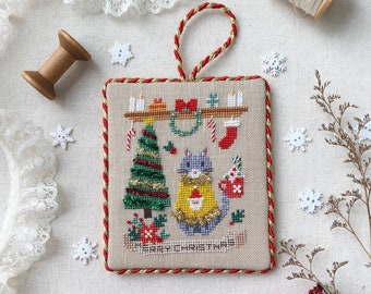 May include: Cross stitch pattern featuring a cat wearing a Christmas sweater with a tree and the words "Merry Christmas". The pattern is framed with a red and gold border and is ready to be stitched.
