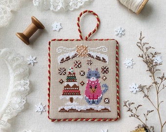 May include: A cross-stitched Christmas ornament from the "Christmas Sweater Series" featuring a gingerbread theme. The ornament has a red and gold border, a red and gold hanging loop, and a design of a gingerbread house and a bird wearing a sweater. The text "Christmas Sweater Series Gingerbread" is at the bottom.