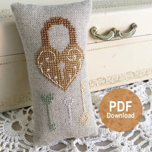 May include: A small, beige pillow with a cross-stitch design of a heart-shaped lock and three keys. The pillow is sitting on a white crocheted doily. The text "PDF Download" is visible in the lower right corner of the image.