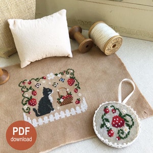 May include: Cross stitch pattern featuring a black cat sitting in a field of strawberries. The pattern is on a beige fabric and includes a small round ornament with a similar design. The text "PDF download" and "Stitch with Coffee on Etsy" are also visible.