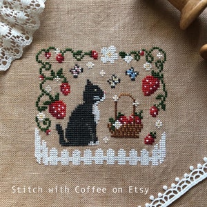May include: Cross-stitch pattern of a black cat sitting in a garden with strawberries, flowers, and butterflies. The text "homestead" is stitched below the cat. The pattern is on a beige linen fabric.