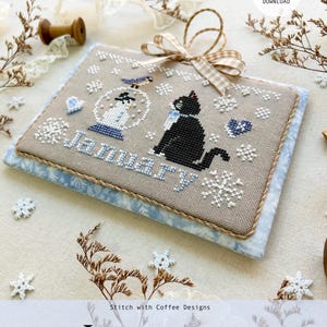 May include: Cross stitch pattern for a January 2025 calendar featuring a black cat and a snowman in a snow globe. The pattern is titled "January" and is part of a monthly kitty calendar series. The pattern is available as a PDF download.