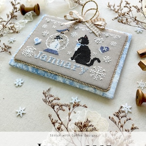May include: A cross-stitch pattern for a January 2025 calendar featuring a black cat and a snowman inside a snow globe. The design is titled "Monthly Kitty Calendar Series 2025" and is by Stitch with Coffee Designs.