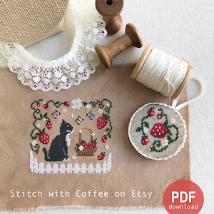 May include: Cross stitch pattern featuring a black cat sitting near a basket of strawberries. The pattern is surrounded by a border of green vines and white flowers. The pattern is on a beige fabric with a white background. The text "Stitch with Coffee on Etsy" is at the bottom of the image. The text "PDF download" is in a red circle at the bottom right of the image.