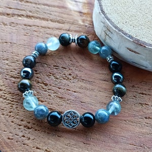May include: A beaded bracelet with black, green, and blue stones. The bracelet has a silver charm with a decorative design.