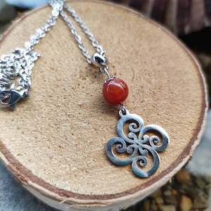 May include: A silver necklace with a red carnelian bead and a silver pendant with a Celtic knot design.