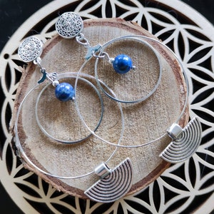 Peut inclure: Une paire de boucles d'oreilles créoles en argent avec un pendentif en lapis-lazuli sur chaque créole. Les créoles sont superposées et ont un charme décoratif en demi-cercle suspendu au bas.