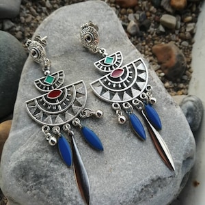 Peut inclure: Boucles d'oreilles pendantes argentées avec des accents bleus, rouges et verts. Les boucles d'oreilles présentent un design géométrique avec un sommet circulaire et plusieurs pendentifs en forme de goutte.