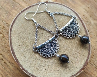 May include: Silver dangle earrings with a delicate filigree design and a dark brown stone pendant.