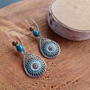 May include: A pair of silver teardrop earrings with a blue and white patterned design. Each earring features a brown tiger's eye bead and a blue bead.