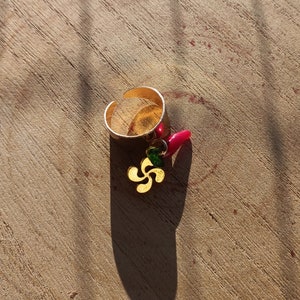 Peut inclure: Une bague en or avec un charme rouge et vert suspendu. Le charme est un trèfle à quatre feuilles stylisé.