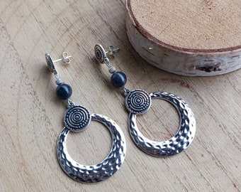May include: A pair of silver dangle earrings with a hammered metal circle and a smaller circle with a concentric circle design. The earrings are accented with dark blue beads.
