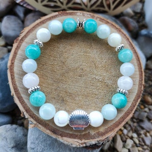Peut inclure: Un bracelet en perles turquoise et blanches avec un charme en forme de coquillage argenté. Le bracelet est composé de perles rondes et possède un fermoir argenté.