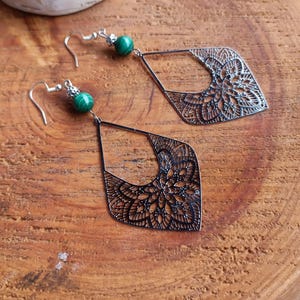 Peut inclure: Une paire de boucles d'oreilles pendantes en argent avec une perle de malachite verte sur chaque boucle d'oreille. Les boucles d'oreilles présentent un design délicat et complexe en filigrane.