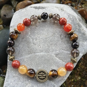 Peut inclure: Un bracelet composé de perles rouges, orange, brunes et noires. Le bracelet est doté d'un fermoir en métal avec un motif décoratif.