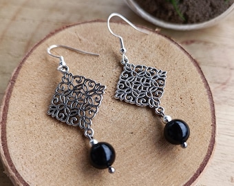 May include: A pair of silver filigree earrings with black bead accents. The earrings feature a square design with intricate details.