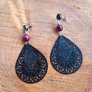 Op de afbeelding: Een paar zwarte filigrein oorbellen met een roze en zwarte edelsteen accent.