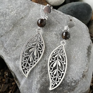 Peut inclure: Boucles d'oreilles en forme de feuille en filigrane argent avec des perles de pierres précieuses brunes. Les boucles d'oreilles sont suspendues à un poteau argenté.