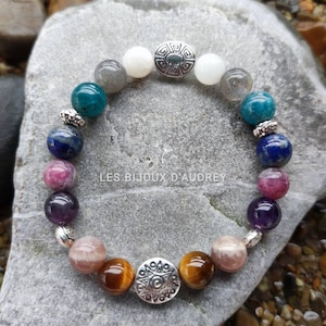 May include: A bracelet with a variety of colorful gemstones, including amethyst, tiger's eye, and moonstone. The bracelet has two silver charms with geometric designs.