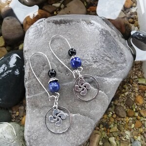 Puede incluir: Un par de pendientes de plata con cuentas azules y negras y un dije de plata en forma de trébol de cuatro hojas.