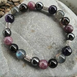 Peut inclure: Un bracelet composé de perles d'améthyste, de labradorite, de quartz fumé, d'hématite et de lépidolite. Le bracelet est orné d'entretoises argentées entre chaque perle.
