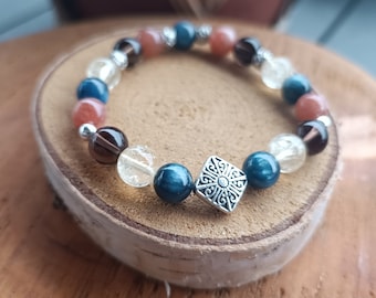 May include: A beaded bracelet with blue, brown, and orange stones, and a silver charm with a geometric design.
