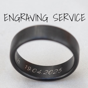 以下が含まれることがあります： 黒色のジルコニウムリング。リングの上には「ENGRAVING SERVICE」の文字。リングの内側には日付「19.04.2025」が刻まれています。「Inside engraving service for black zirconium rings」の文字が下にあります。